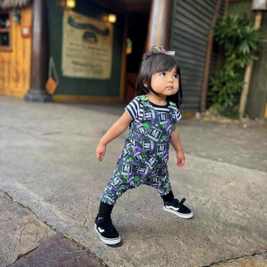 Goth toddler wearing spooky kid clothes, romper with beetlejuice print on it. Striped t-shirt.