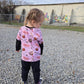 Child wearing a pink shirt with graphics on a gravel surface with graffiti in the background