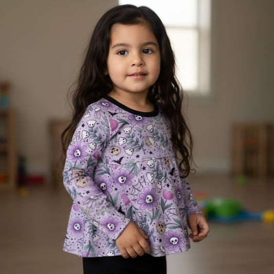 Young girl wearing a spooky purple floral long-sleeve shirt in a room with toys on the floor.