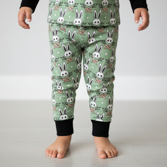 Child wearing green pajama pants with bunny pattern on a plain background