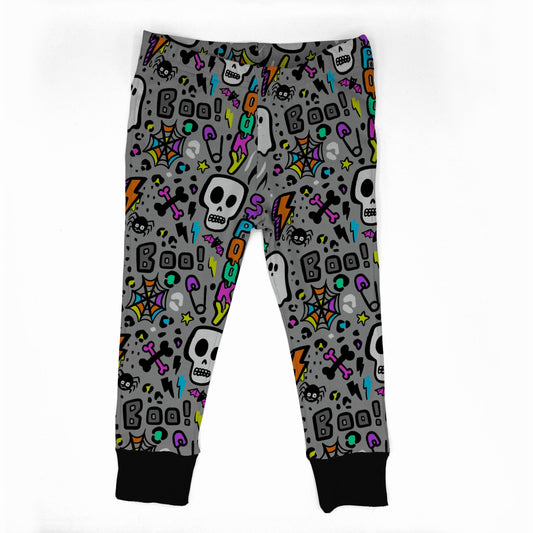 Gray children's jogger pants with a colorful Halloween pattern featuring skulls, ghosts, spiders, and 'Boo!' text, finished with black ribbed cuffs.